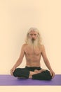 Studio shot of senior bearded man sitting on yoga mat with legs crossed shirtless Royalty Free Stock Photo