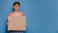 Studio shot of a smiling young woman holding a blank cardboard sheet on a blue background. Copy space, space for your ad Royalty Free Stock Photo