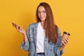 Studio shot of smiling young woman holding mobile phone and drinking take away coffee, surfing interner or chatting with friends, Royalty Free Stock Photo