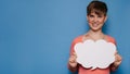 Studio shot of a smiling young woman holding a white empty banner in the form of a cloud on a blue background. Copy Royalty Free Stock Photo