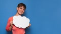 Studio shot of a smiling young woman holding a white empty banner in the form of a cloud on a blue background. Copy Royalty Free Stock Photo