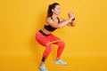 Studio shot of sporty woman squatting, doing sit ups with resistance band. Photo of Caucasian woman in fashionable sportswear