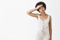 Studio shot of tired gloomy hardworking female office worker in white overalls whiping sweat out of forehead and gazing