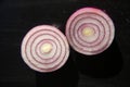 Studio shot of two halfs of round sliced vitamin red onion vegetable rings on a black textured background close up, top view Royalty Free Stock Photo
