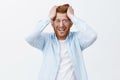 Studio shot of upset redhead man in despair and shook, feeling distressed losing company, pulling hair out of head