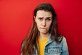 Studio shot of upset young woman purses lower lip, pouting and has displeased look, looks sadly at camera, wears denim jacket,