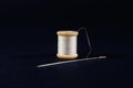 Studio shot of a white thread reel and a sewing needle on a black background. Spool (or reel), thread needle are used Royalty Free Stock Photo