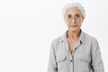 Studio shot of wise and intelligent skillful senior female doctotr in glasses with gray hair standing calm and confident