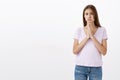 Studio shot of woman feeling guilty holding hands in pray purisng lips and frowning while asking forgiveness from friend Royalty Free Stock Photo