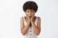 Studio shot of worried intense african american female employee with afro hairstyle holding palms on cheeks and frowning