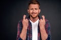 Studio shot of worried intense redhead miserable guy with beard in blue shirt crossing fingers, pursing lips and frowning while