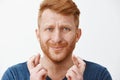 Studio shot of worried intense redhead miserable guy with beard in blue t-shirt crossing fingers, pursing lips and