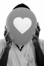 Face of young black African man patient hiding face behind balloon with heart sign