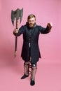 Studio shot of young bearded man in image of medieval warrior, archery in chain armor with ax isolated over pink Royalty Free Stock Photo