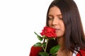 Studio shot of young beautiful Brazilian woman smelling red rose Royalty Free Stock Photo