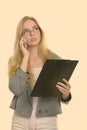 Thoughtful young businesswoman holding clipboard and talking on mobile phone Royalty Free Stock Photo