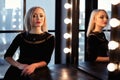 Studio shot of young and beautiful girl standing near mirror in black dress wearing in studio. Blonde girl Royalty Free Stock Photo