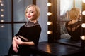 Studio shot of young and beautiful girl standing near mirror in black dress wearing in studio. Blonde girl Royalty Free Stock Photo