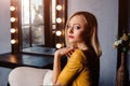 Studio shot of young and beautiful girl standing near mirror in yellow leather dress wearing in studio. Blonde girl Royalty Free Stock Photo