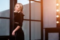 Studio shot of young and beautiful girl standing near window in black dress wearing in studio. Blonde girl Royalty Free Stock Photo