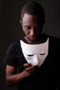 Studio shot of young black African man in dark room holding mask Royalty Free Stock Photo