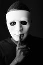 Studio shot of young black African man in dark room wearing mask and holding finger on lips Royalty Free Stock Photo
