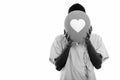 Studio shot of young black African man patient hiding face behind balloon with heart sign