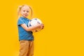 Studio shot of young blonde girl holding soccer ball against yellow background. Child and football. Copy space, mockup Royalty Free Stock Photo