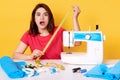 Studio shot of young brunette dressmaker in panic after making mistake while sewing new outfit, lady wearing red casual t shirt,