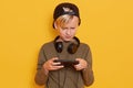 Studio shot of young caucasian little boy using mobile phone against yellow studio background, guy looks concentrated, holding his Royalty Free Stock Photo