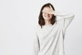 Studio shot of young cute european girl, covering her eyes with hand while smiling cheerfully, being impatient. Mom told