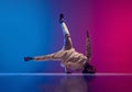 Studio shot of young flexible sportive man dancing breakdance in white outfit on gradient pink blue background. Concept