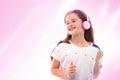 Studio shot of a young girl  on a color background.  She is standing in pink headphones listening to music and smiling Royalty Free Stock Photo