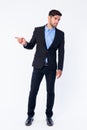 Full body shot of young bearded Persian businessman pointing to side and looking away Royalty Free Stock Photo