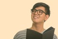 Studio shot of young happy Asian man smiling while holding book and thinking Royalty Free Stock Photo