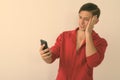 Studio shot of young handsome man having headache while using mobile phone against white background Royalty Free Stock Photo