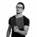 Studio shot of young handsome man holding book while thinking with eyeglasses isolated against white background Royalty Free Stock Photo