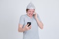 Stressed young man with tin foil hat using phone and having headache Royalty Free Stock Photo