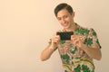 Studio shot of young happy tourist man smiling while taking picture with mobile phone against white background Royalty Free Stock Photo