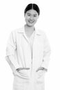 Studio shot of young happy Asian woman doctor smiling with hands on pockets Royalty Free Stock Photo