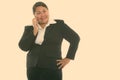 Studio shot of young happy fat Asian businesswoman smiling while talking on mobile phone with hand on hip Royalty Free Stock Photo