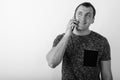 Studio shot of young happy muscular man smiling and thinking while talking on mobile phone against white background Royalty Free Stock Photo