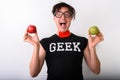 Studio shot of young happy nerd man smiling while holding red ap Royalty Free Stock Photo