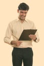 Studio shot of young happy Persian businessman smiling while reading on clipboard Royalty Free Stock Photo