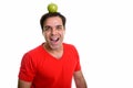 Studio shot of young happy Persian man smiling with green apple Royalty Free Stock Photo