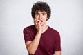 Studio shot of young man with dark curly hair, dressed casually, biting fingernails and looking looking directly at camera while