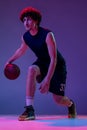 Studio shot of young muscular basketball street player dribbling ball isolated on purple background in neon. Concept of Royalty Free Stock Photo