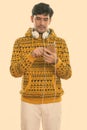 Studio shot of young Persian man wearing headphones around neck and using mobile phone