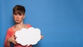 Studio shot of a young woman with a bizarre facial expression, holding a white empty banner in the form of a cloud on a Royalty Free Stock Photo