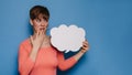 Studio shot of a young woman with a puzzled expression, holding a white empty banner in the form of a cloud on a blue Royalty Free Stock Photo